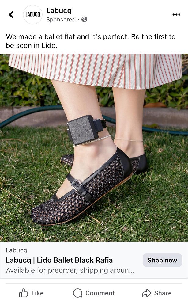 A person wearing black raffia ballet flats and a large electronic ankle monitor, standing on grass in a striped skirt.