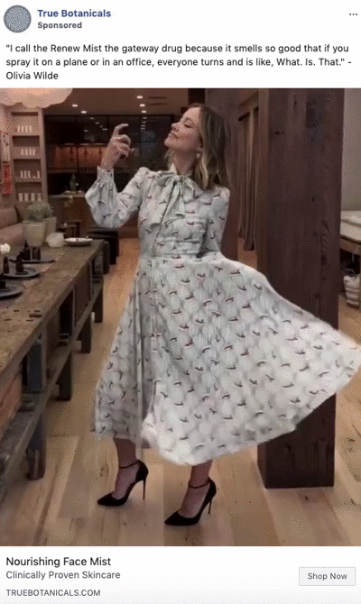A woman in a floral dress poses for a selfie in a wooden-floored boutique, holding a spray bottle, with a quote from Olivia Wilde displayed above.