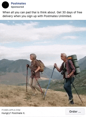 Two people with backpacks and hiking poles walk along a grassy hillside with mountains in the background. Postmates delivery promotion text appears above them.
