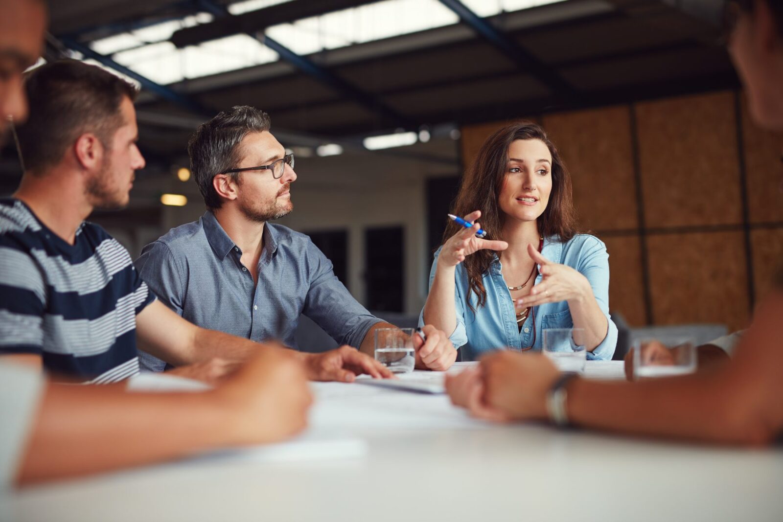 Four people sit at a table having a discussion, with one woman speaking and gesturing while the others listen attentively.