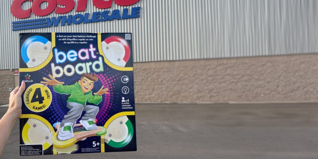 A person holds a "Beat Board" balance game box in front of a Costco Wholesale store exterior, ready to See the True ROI of Your Marketing Mix in action.