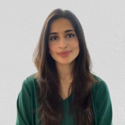 A woman with long brown hair wearing a green top sits in front of a plain white background, looking at the camera with a neutral expression.
